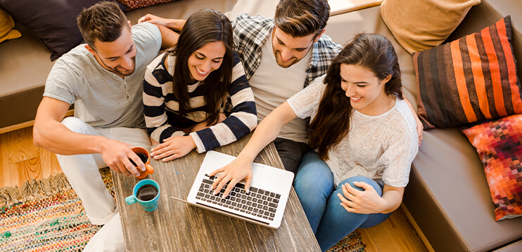 Top view of group of 4 friends around a coffee table , looking at a laptop and having coffee